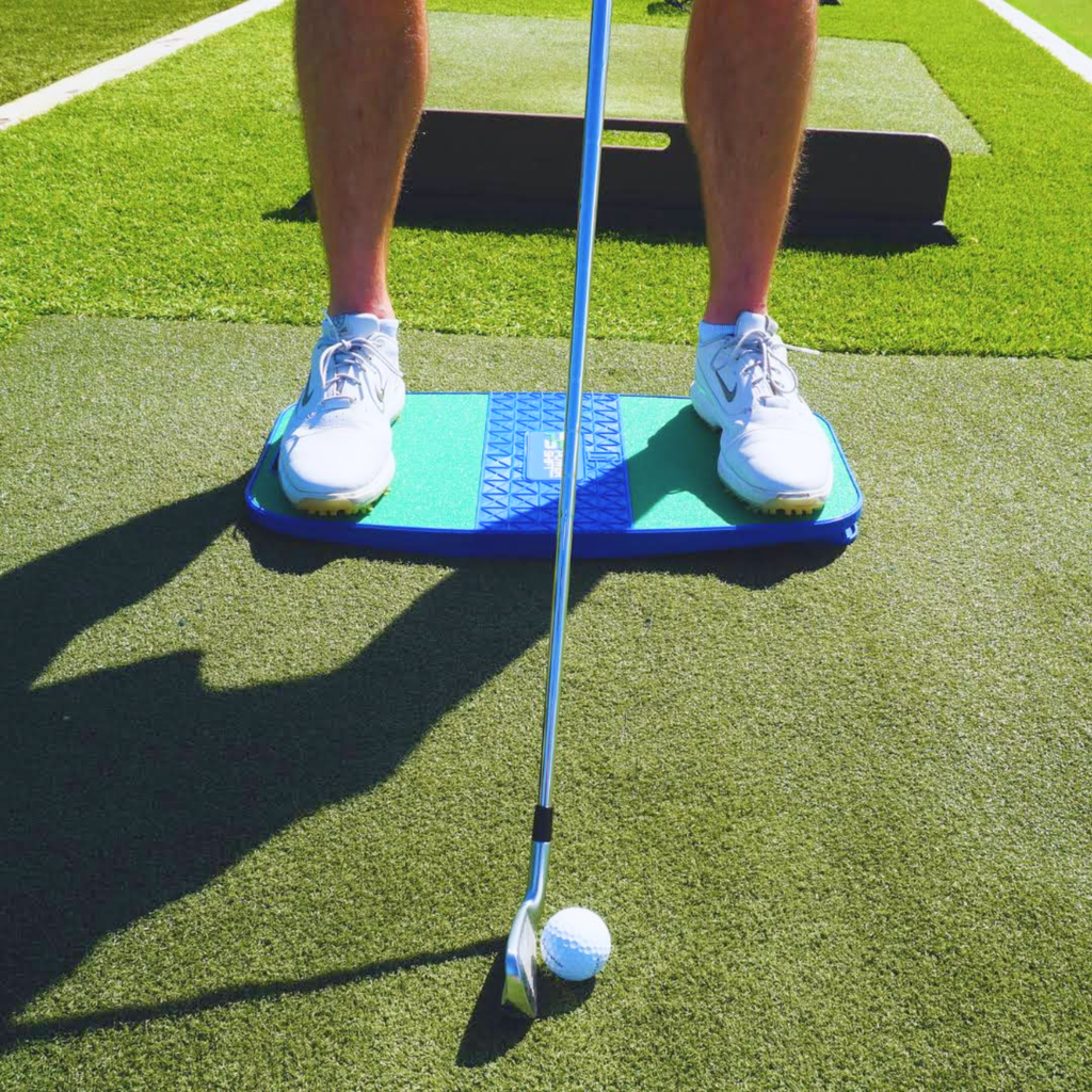 Golfer standing on the Power Shift Board with a club addressing the ball on a practice mat
